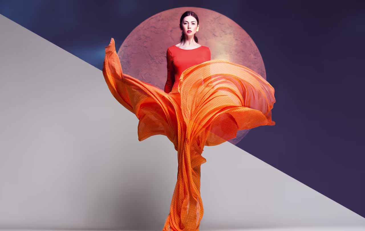 Model in a flowing orange dress posed in front of a large circular backdrop, styled with Optics photographic looks