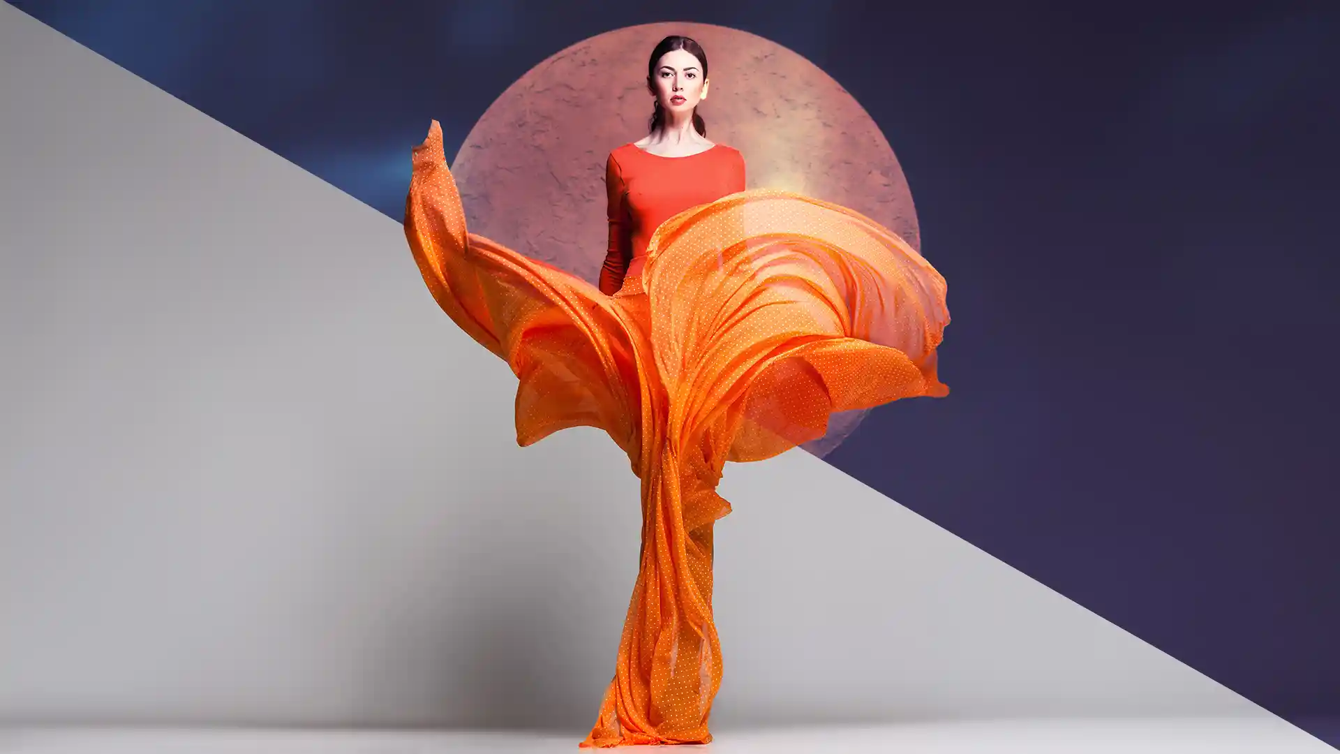 Model in a billowing orange dress against a split grey and navy backdrop, created in Optics.